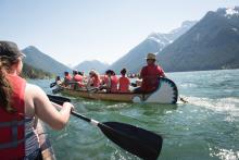 group of young people canoeing in water surrounded by mountains