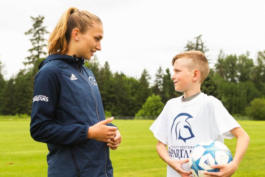 Young boy holding a soccerball at a TWU summer camp, talking to an older female soccer player.