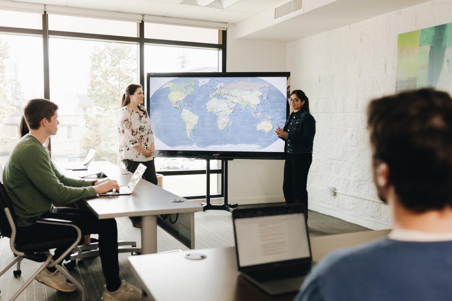 students in a classroom with a professor explaining a map on display