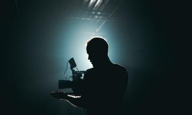 person in darkness with video camera who is backlit with white light