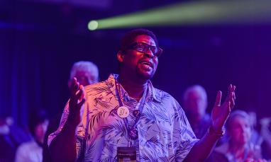 man singing with hands raised in a dark room with colourful lights
