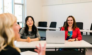 two professors smiling with a laptop in front of them