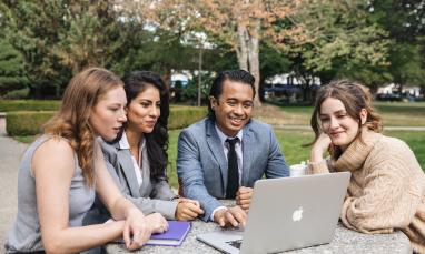 people sitting at a table outside around a laptop