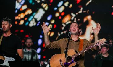 Worship leader with a guitar holding his hands up in praise