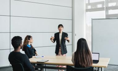 Professionally dressed instructor teaching three students in a white room