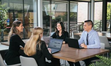 Four people sitting at a desk working or talking