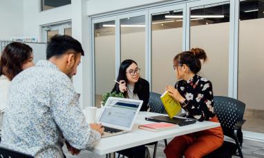 Four people sitting at a desk working or talking