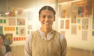 Aliya standing in a room of paintings smiling at the camera