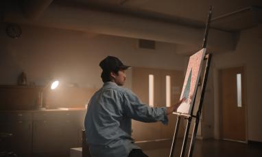 A student painting in a dimly lit room
