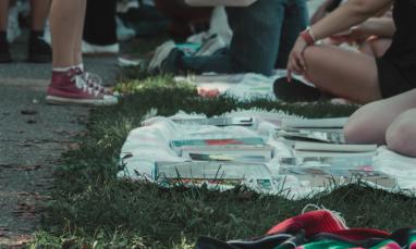 Students gathered outdoors, sitting and standing on grass with books laid out on blankets.