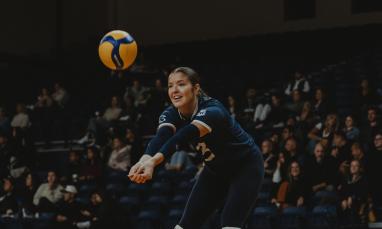 Volleyball player in a dark blue uniform prepares to receive the ball with arms extended.