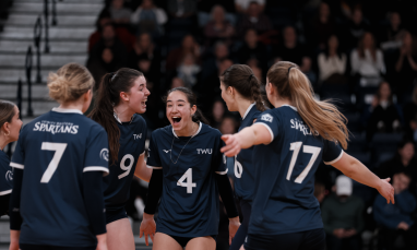  TWU Spartans volleyball players huddle joyfully in blue jerseys.