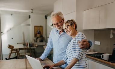 Elderly couple smiling and using laptop at kitchen counter