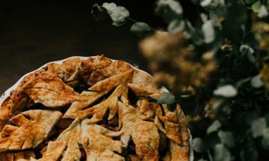 Golden-brown pie with leaf-shaped crust, beside blurred greenery.