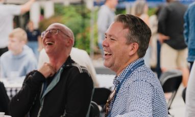 Two men laughing together at an outdoor event.