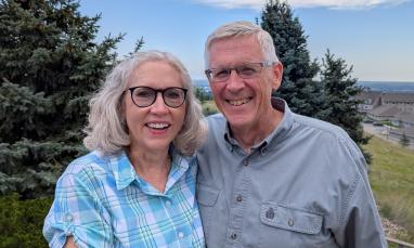 Smiling couple outdoors with trees and clear sky.