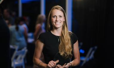 Smiling woman holding an award, standing in a dimly lit room.