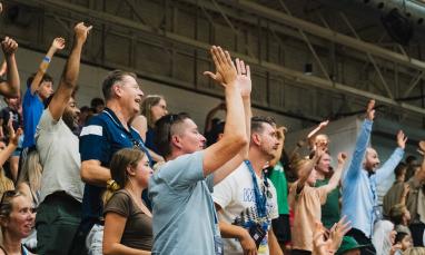 Cheering crowd in a stadium with raised arms, showing excitement and energy.