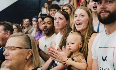 Crowd cheering at an indoor event, mixed ages and expressions of excitement.