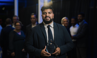 Man in a suit holding an award, standing in front of a group at an event.