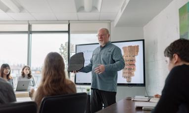 A New Testament professor teaches students in a classroom with a slide displaying an ancient manuscript.