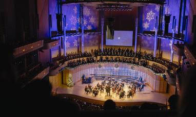 Concert hall with orchestra, choir, and blue-lit snowflake decorations.