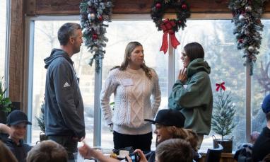 People standing indoors by decorated windows with wreaths.