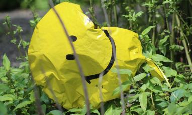 Deflated yellow smiley balloon in green foliage.