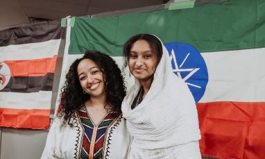 Two people smiling in front of Ethiopian and Ugandan flags.