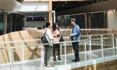 Three people talking in a bright, modern office hallway.