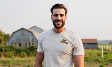 Man smiling in front of a farm with barns.