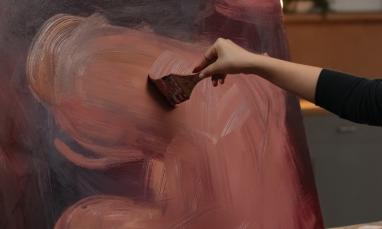 Hand painting large brushstrokes on canvas with earthy tones.