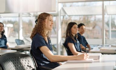 Students attentively listening in a sunlit classroom.