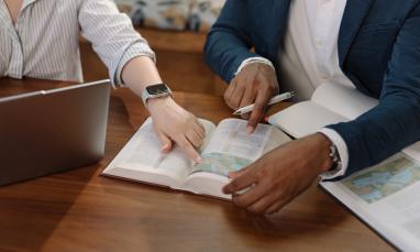 Two people pointing at a Bible, working together at a table.