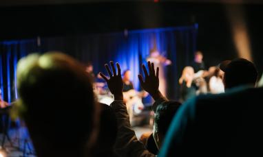 Concert audience with hands raised, spotlight on stage.