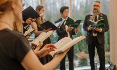 TWU Chamber Choir hold songbooks and sing with plastic coloured lights draped around their shoulders.
