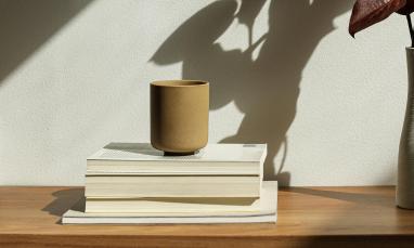 A brown cup sits on a stack of books next to a vase of purple plants.