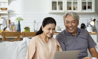Couple seated on sofa and smiling while looking at laptop