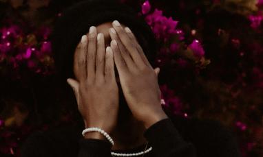 Man covering his face with his hands with a bright pink bush of flowers in the background