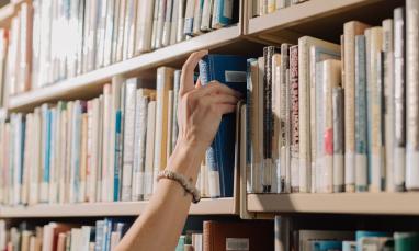 hand grabbing a book of a library bookshelf