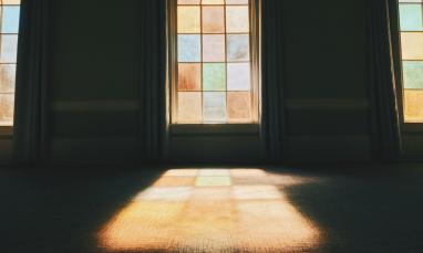 Sunlight streaming through tall arched stained‑glass windows, casting colorful light onto the floor of a dimly lit room.