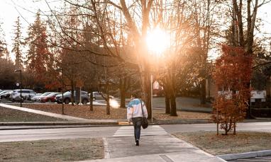 person walking away from the camera towards a setting sun on campus
