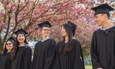 graduates in regalia walking in front of cherry blossoms
