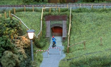 Miniature scene of a person on a bicycle approaching a small brick tunnel under a grassy embankment.