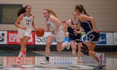 Girls in white and blue jerseys playing basketball.