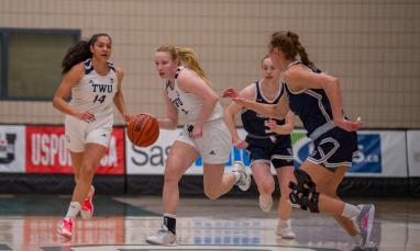 Girls in white and blue jerseys playing basketball.