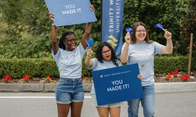 Three TWU students holding welcome signs during orientation day on the Langley campus.