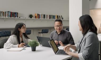 Students and faculty discussing coursework together around a table in a classroom setting.