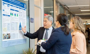 A presenter discusses a research poster with two attendees during a poster presentation.
