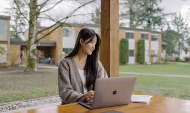 Student working on a laptop at an outdoor table on the TWU campus.
